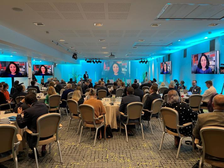 People sitting around tables in room full of presentation screens. 