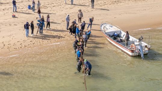 people and a small boat on the shore of the beach