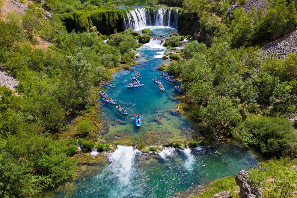 Small boats approach a pristine blue river and waterfall in Croatia